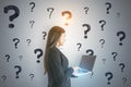 Portrait of attractive thoughtful young european businesswoman with laptop standing on concrete wall background with question