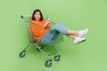 Portrait of attractive trendy cheerful girl riding cart using device smm blogging isolated over bright green color