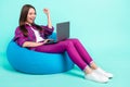 Portrait of attractive trendy cheery girl lying in bag chair using laptop having fun rejoicing isolated over bright teal Royalty Free Stock Photo