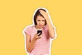 Portrait of attractive unhappy girl in striped T-shirt looking at smart phone in her arm with shocked, holding hand on head. WTF