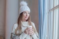 Portrait of attractive winter woman in season casual clothes white sweater and knitted hat at cozy home