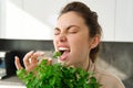 Portrait of attractive woman biting parsley, eating fresh vegetables and herbs in the kitchen, enjoying healthy Royalty Free Stock Photo