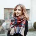 Portrait of an attractive woman with blond hair with a wonderful smile in a black stylish coat with a woolen checkered warm scarf
