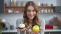 Portrait of attractive woman choosing between cake and apple at home kitchen. Royalty Free Stock Photo