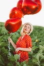 Portrait of attractive woman in red dress posing with heart-shaped balloons on green nature background. Girl in straw Royalty Free Stock Photo