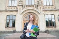 Portrait of attractive woman standing against a university building with coffee and books in her hands Royalty Free Stock Photo