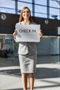 Portrait of attractive woman standing while holding white board with Check in signage  at airport Royalty Free Stock Photo