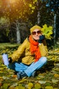 Portrait of attractive woman on a walk in autumn park sitting on yellow foliage in sunlight. Pretty girl holding maple leaves and Royalty Free Stock Photo