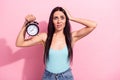 Portrait of attractive worried funky long-haired girl holding clock oops over pink pastel color background