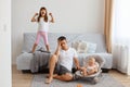 Portrait of attractive young adult man sitting on floor near sofa with his infant girl in rocking chair, being tired of loud elder Royalty Free Stock Photo