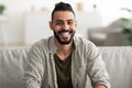 Portrait of attractive young Arab man smiling and looking at camera, sitting on couch at home Royalty Free Stock Photo