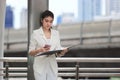 Portrait of attractive young Asian business woman holding mobile smart phone and ring binder at outside office Royalty Free Stock Photo