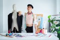 Portrait of attractive young Asian LGBTQ gay dressmaker standing confident pose with mannequin behind working desk, sketch of Royalty Free Stock Photo