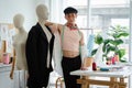 Portrait of attractive young Asian LGBTQ gay dressmaker standing confident pose with mannequin near working desk, sketch of Royalty Free Stock Photo