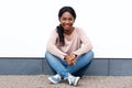 Attractive young black woman sitting on floor and smiling against white wall Royalty Free Stock Photo