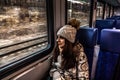 Winter close-up portrait of beautiful young female looks out the train window. girl in winter clothes goes on vacation. She is Royalty Free Stock Photo