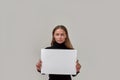 Portrait of attractive young caucasian woman looking at camera, holding white blank banner in front of her while Royalty Free Stock Photo