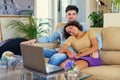 Attractive young couple sits on a couch with a laptop on a table in a living room.