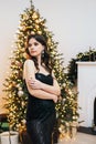 Portrait of an attractive young girl in a black dress. Sexy dressed young woman posing on the background of a Christmas tree. Royalty Free Stock Photo