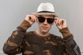 Portrait of an attractive young hipster man in black trendy sunglasses in a military green stylish shirt in a vintage hat Royalty Free Stock Photo