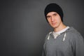 Portrait of an attractive young male model in black hat, jeans and gray sweatshirt, studio, dark gray background Royalty Free Stock Photo