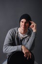 Portrait of an attractive young male model in black hat, jeans and gray sweatshirt, studio, dark gray background Royalty Free Stock Photo