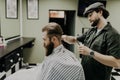 Portrait of attractive young man getting trendy haircut. Male hairdresser serving client, making haircut using metal scissors and Royalty Free Stock Photo