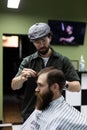 Portrait of attractive young man getting trendy haircut. Male hairdresser serving client, making haircut using metal scissors and Royalty Free Stock Photo