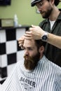 Portrait of attractive young man getting trendy haircut. Male hairdresser serving client, making haircut using metal scissors and Royalty Free Stock Photo