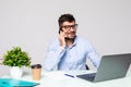 Portrait of attractive young man in glasses sitting at office desk with laptop computer and talking on mobile phone. Communication Royalty Free Stock Photo