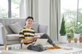 Portrait of an attractive young man sitting on a floor at the couch in the living room, using laptop computer Royalty Free Stock Photo