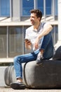 Attractive young man sitting outdoors with mobile phone and laughing Royalty Free Stock Photo