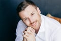 Portrait of attractive young unshaven Caucasian male with stubble, has positive look, keeps hands under chin, dressed in elegant w Royalty Free Stock Photo