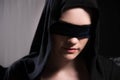 Portrait of an attractive young woman in a black hood and blindfolded with a black bandage in a dark room. Low key Royalty Free Stock Photo