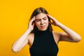 Portrait of attractive young woman with brunette hair has headache, bursting with thoughts.  on yellow background, studio Royalty Free Stock Photo