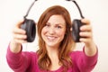 Hear, have a listen to this. Portrait of an attractive young woman offering you a pair of headphones.