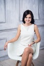 Portrait of attractive young woman sitting in a chair. elegant white dress. White floor and white wall in the background