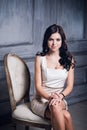 Portrait of attractive young woman sitting in a chair. elegant white dress. White floor and white wall in the background Royalty Free Stock Photo