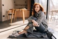 Portrait of attractive young woman sitting by window on sunny day relaxing at home, smiling looking at camera, holding Royalty Free Stock Photo