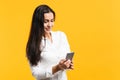 Portrait of attractive young woman in white casual shirt using mobile phone and typing sms message  on yellow Royalty Free Stock Photo