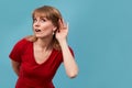 Portrait of an attrative long hair young woman making what did you say sign by putting her hand to her ear wearing red Royalty Free Stock Photo