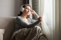 Portrait of ÃÂaucasian young woman in headphones listening music sitting on sofa covered blanket, drinking coffee from cup Royalty Free Stock Photo