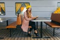 Portrait of awesome girl, wearing coat and yellow beret. Sitting on the train station read a book and looking straight. Autumn