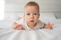 Portrait of a baby with blue eyes lying on a white bed, dressed in a bodysuit, caring for a 6 month old baby, an infant Royalty Free Stock Photo