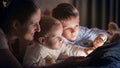 Portrait of baby boy using tablet computer with brother and mother in bed at night. Family having time together, parenting, happy Royalty Free Stock Photo