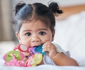 Portrait, baby girl and biting toys in bedroom, house and home for development, growth and teething progress. Cute kid