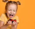 Closeup of young baby girl kid with a handful of berries fruits in her palms hands laughing screaming on yellow