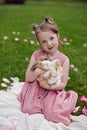 portrait baby girl in a pink dress plays with a rabbit in a green meadow in summer. Funny friendship between a child and Royalty Free Stock Photo