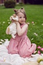 portrait baby girl in a pink dress plays with a rabbit in a green meadow in summer. Funny friendship between a child and Royalty Free Stock Photo