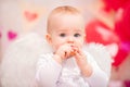 Portrait of a baby girl with white feather wings eating heart-shaped cookies, symbols of Valentine`s Day Royalty Free Stock Photo